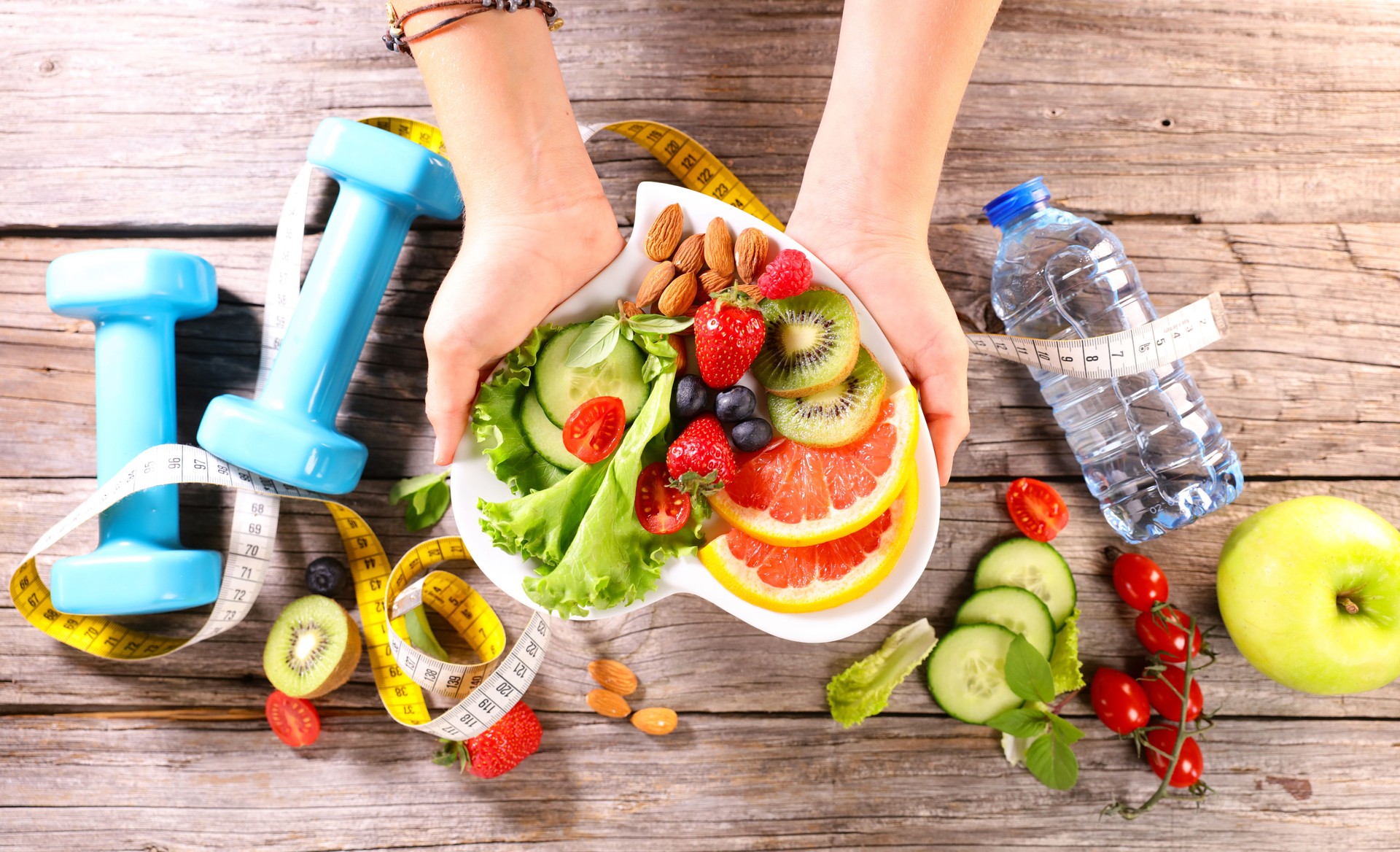 healthy eating concept- hand holding plate with fresh vegetables, dumbell, apple and water- sport health food